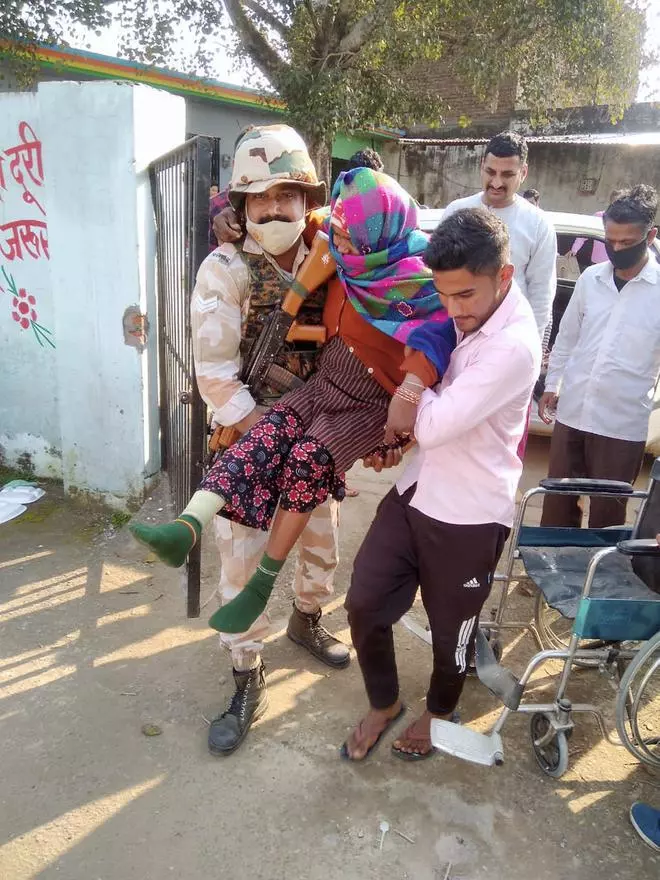Indo-Tibetan Border Police (ITBP) personnel carries a differently-abled woman to the polling booth, during the third phase of UP Assembly elections, in Fatehgarh, on Sunday