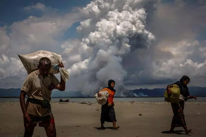 Smoke is seen on the Myanmar border as Rohingya refugees walk on the shore after crossing the Bangladesh-Myanmar border by boat through the Bay of Bengal, in Shah Porir Dwip, Bangladesh September 11, 2017. 