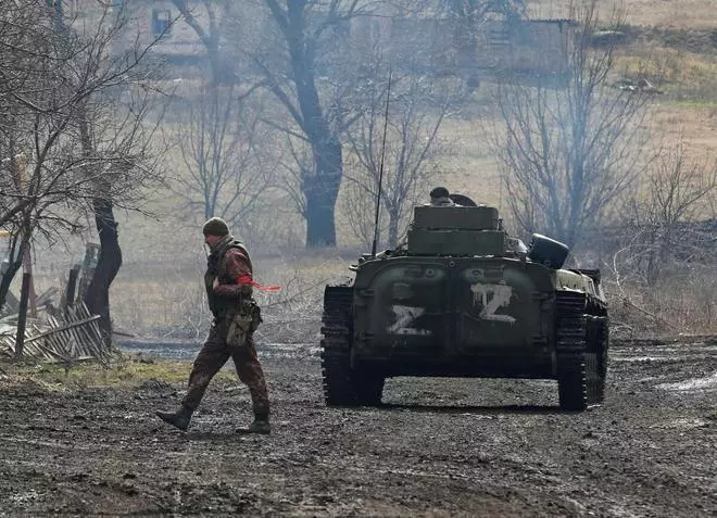 A service member of pro-Russian troops in a uniform without insignia walks next to an armoured vehicle with symbols “Z“ painted on its side in the separatist-controlled village of Bugas during Ukraine-Russia conflict in the Donetsk region, Ukraine March 6, 2022.